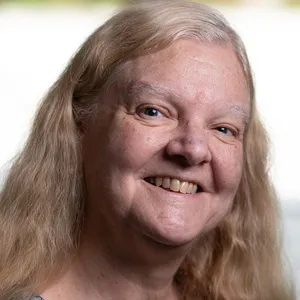 Diane Driedger, with long blonde hair, smiles at the camera in front of a softly blurred indoor background.