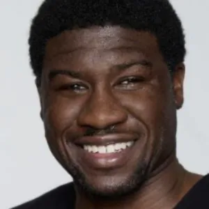 A smiling Ben Akuoko, with short curly black hair and a trimmed goatee, faces the camera in a studio-style headshot, wearing a black T-shirt. 