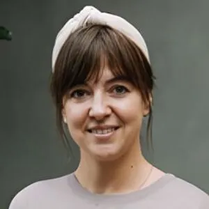 Laura Mudde, with brown hair and bangs, wears a headband and smiles at the camera against a plain background.