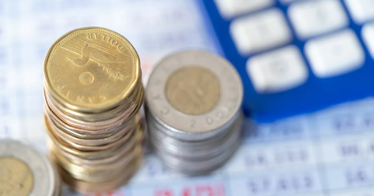 Stack of loonies and toonies on a spreadsheet. A blue calculator is to the right of this pile of coins.