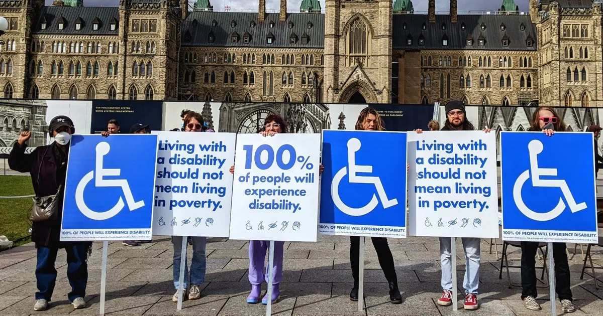 Six people holding signs in front of Parliament