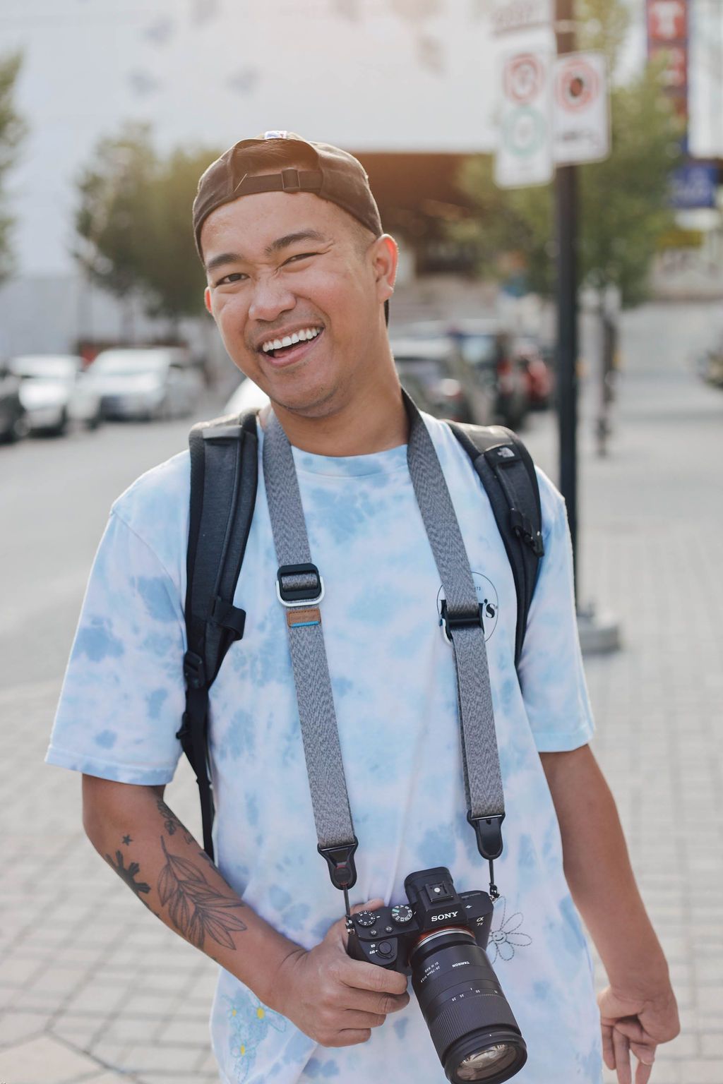 Man in downtown streets with a camera in hand and smiling 