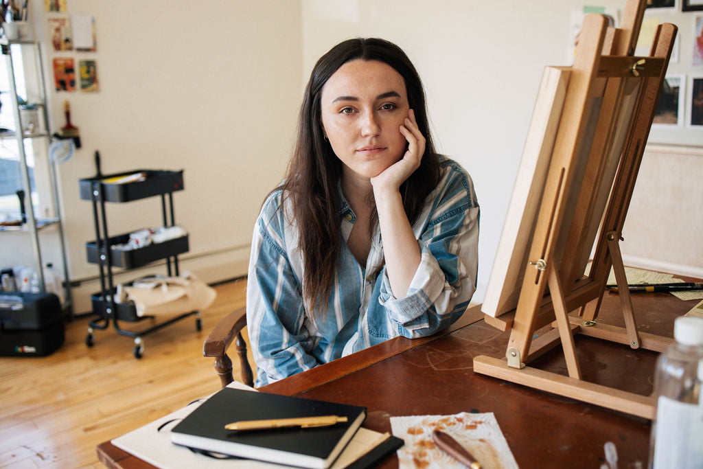 Person sitting in arts space beside easel and book